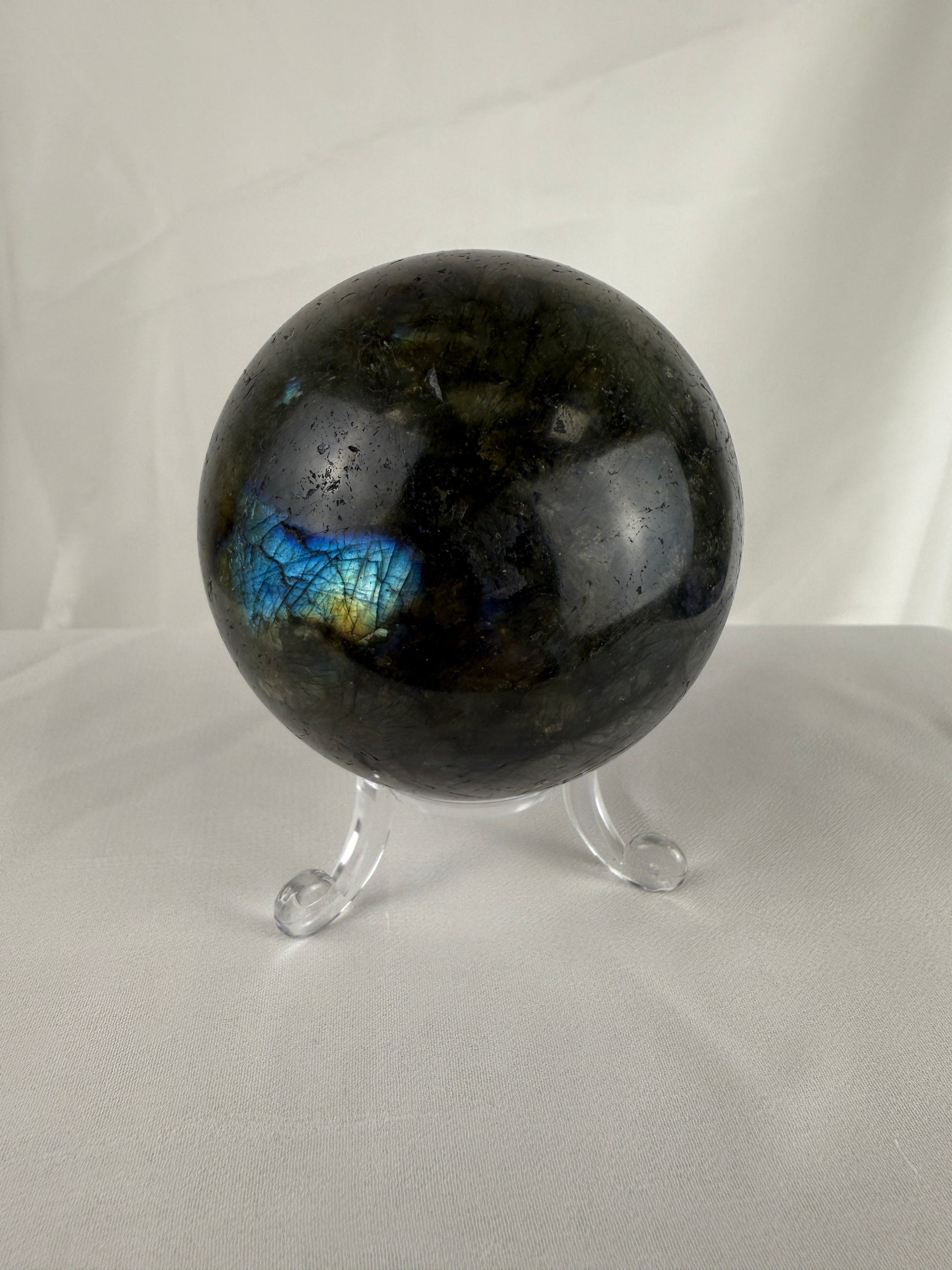 Black labradorite sphere on a stand against a white background